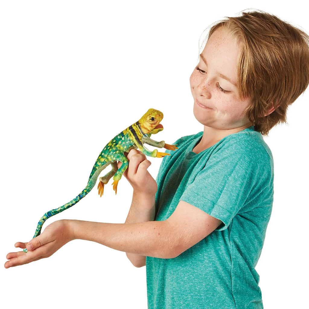 A child in a green shirt holds a colorful toy lizard, smiling with curiosity. The lizard is green with black and yellow stripes, conveying playfulness.