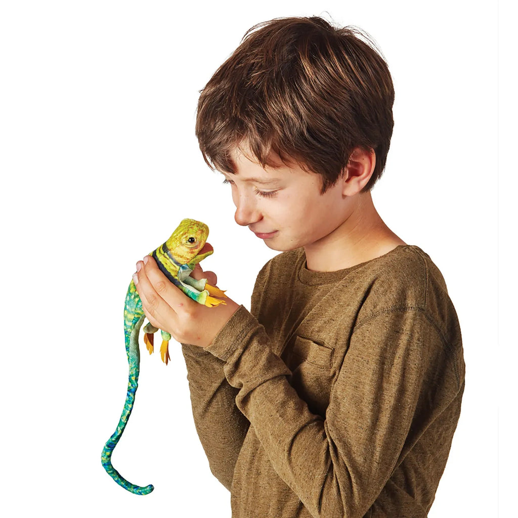 A boy in a brown sweater gently holds a colorful chameleon-like toy, gazing at it with curiosity and affection, against a plain white background.