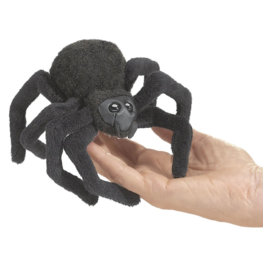 A large, fluffy, black spider toy with cartoonish eyes rests on a person's hand. The playful design creates a friendly and whimsical tone.