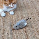 An orange and white cat looking closely at a fluffy plush wind-up mouse toy on a woven mat.