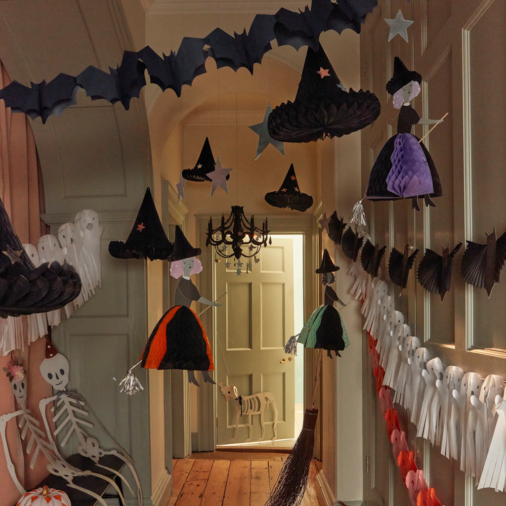 Hallway filled with Halloween decorations, featuring hanging paper witches, bats, ghosts, and skeletons. The atmosphere is spooky yet playful.