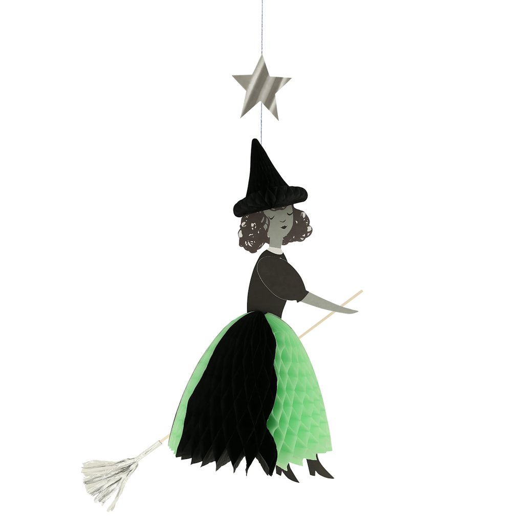 Hanging decoration of a witch on a broomstick, with a green and black honeycomb skirt and pointy hat, beneath a silver star. Playful and whimsical.