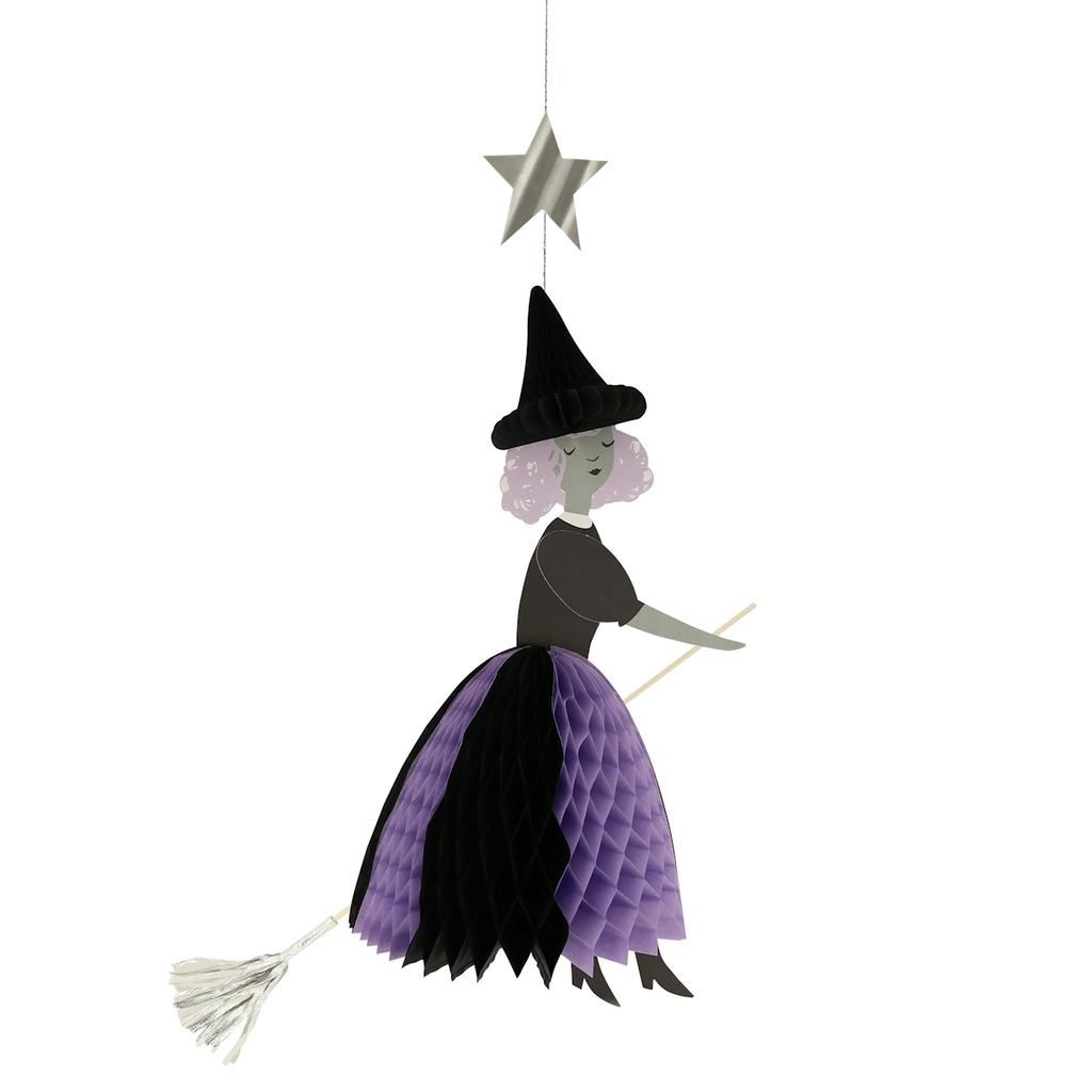 Hanging decoration of a witch on a broomstick, with a purple and black honeycomb skirt and pointy hat, beneath a silver star. Playful and whimsical.