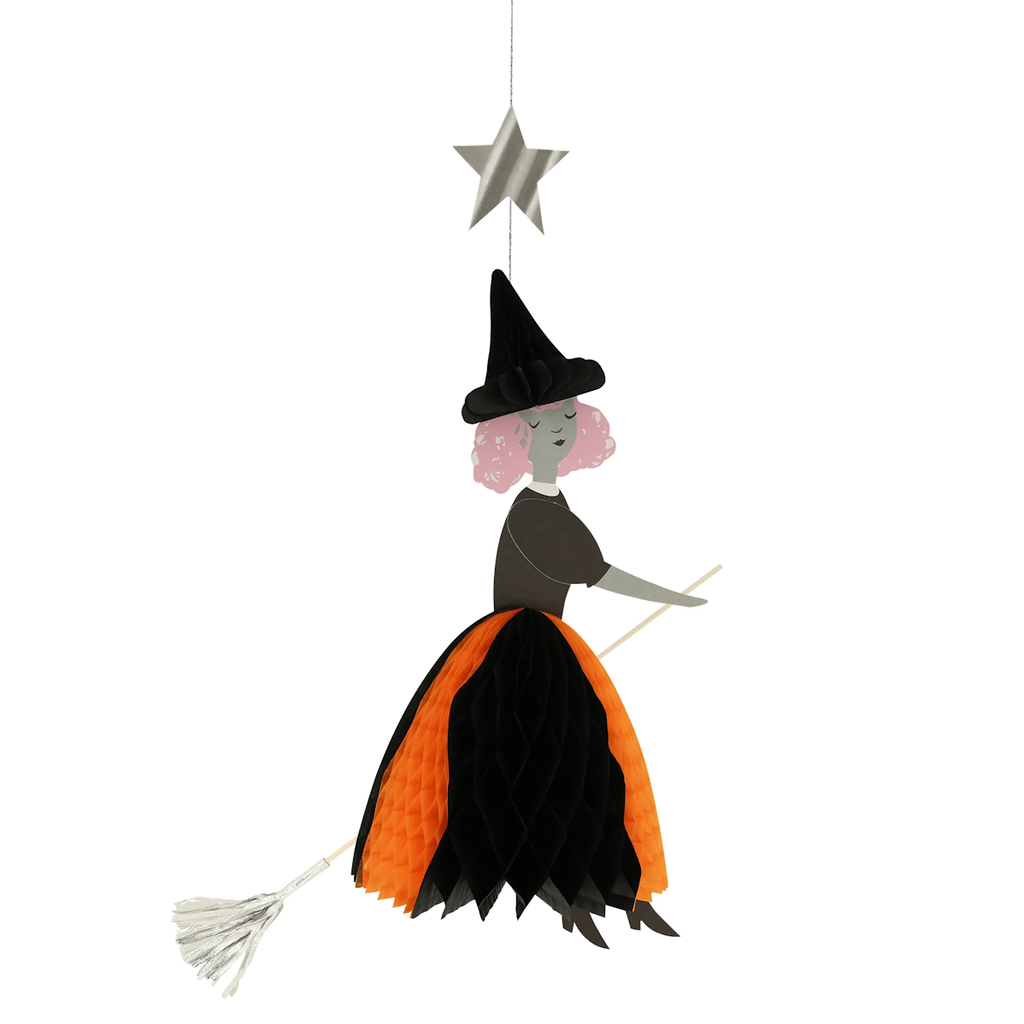 Hanging decoration of a witch on a broomstick, with a orange and black honeycomb skirt and pointy hat, beneath a silver star. Playful and whimsical.