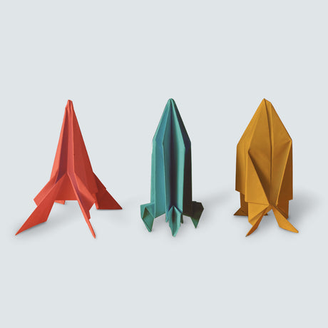 Three colorful origami paper rockets in red, teal, and yellow standing against a light background.
