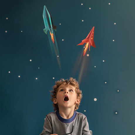 Young boy looking up in awe at two paper rockets launching into space against a starry background.