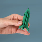 A hand holding a folded green paper rocket against a blue background.