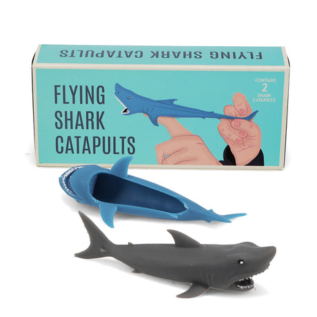 Front packaging and two rubber flying shark finger catapult toys in blue and grey.