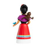 Rear view of a stylized female figurine with a braided bun, wearing a purple shawl, red skirt, and white blouse. A monkey sits on her shoulder, and a blue butterfly rests on her hand. The background is white.