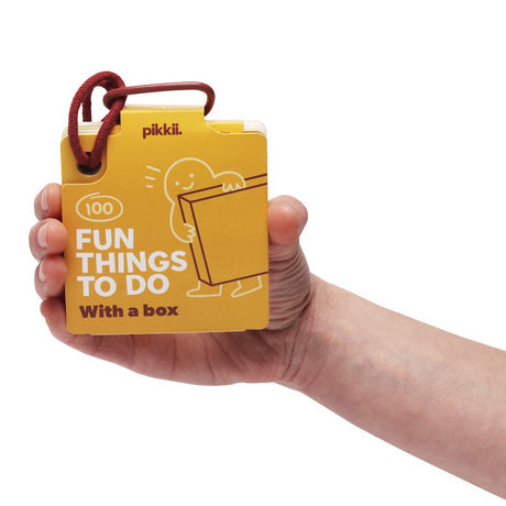 A hand holding a yellow card deck titled "100 Fun Things To Do With a box" on a red cord loop.