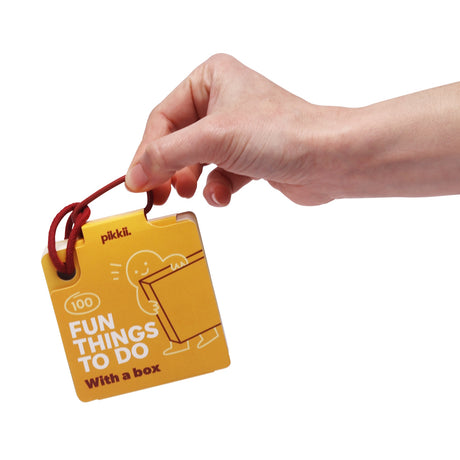 A hand holding pikkii "100 Fun Things To Do With a box" yellow activity card booklet.