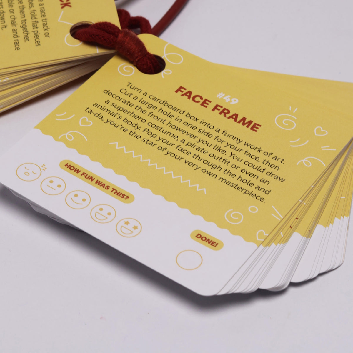 A deck of yellow activity prompt cards bound by a red string showing "Face Frame" activity #49.