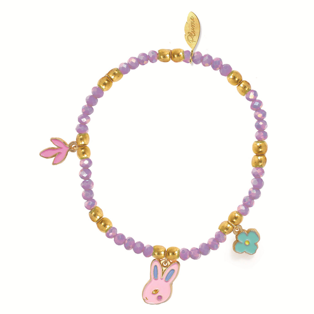 A beaded bracelet features purple and gold beads with charms, a pink bunny, a pink paw, and a blue flower. It has a playful and whimsical tone.