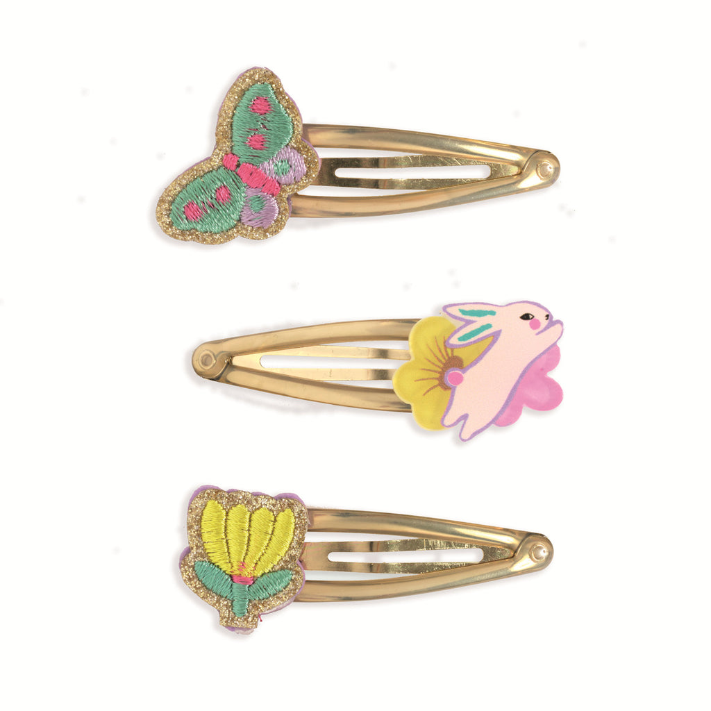 Three decorative gold hair clips are displayed vertically. The top features a colorful butterfly, the middle a pink bunny with a yellow flower, and the bottom a yellow flower with green leaves. Bright and whimsical.