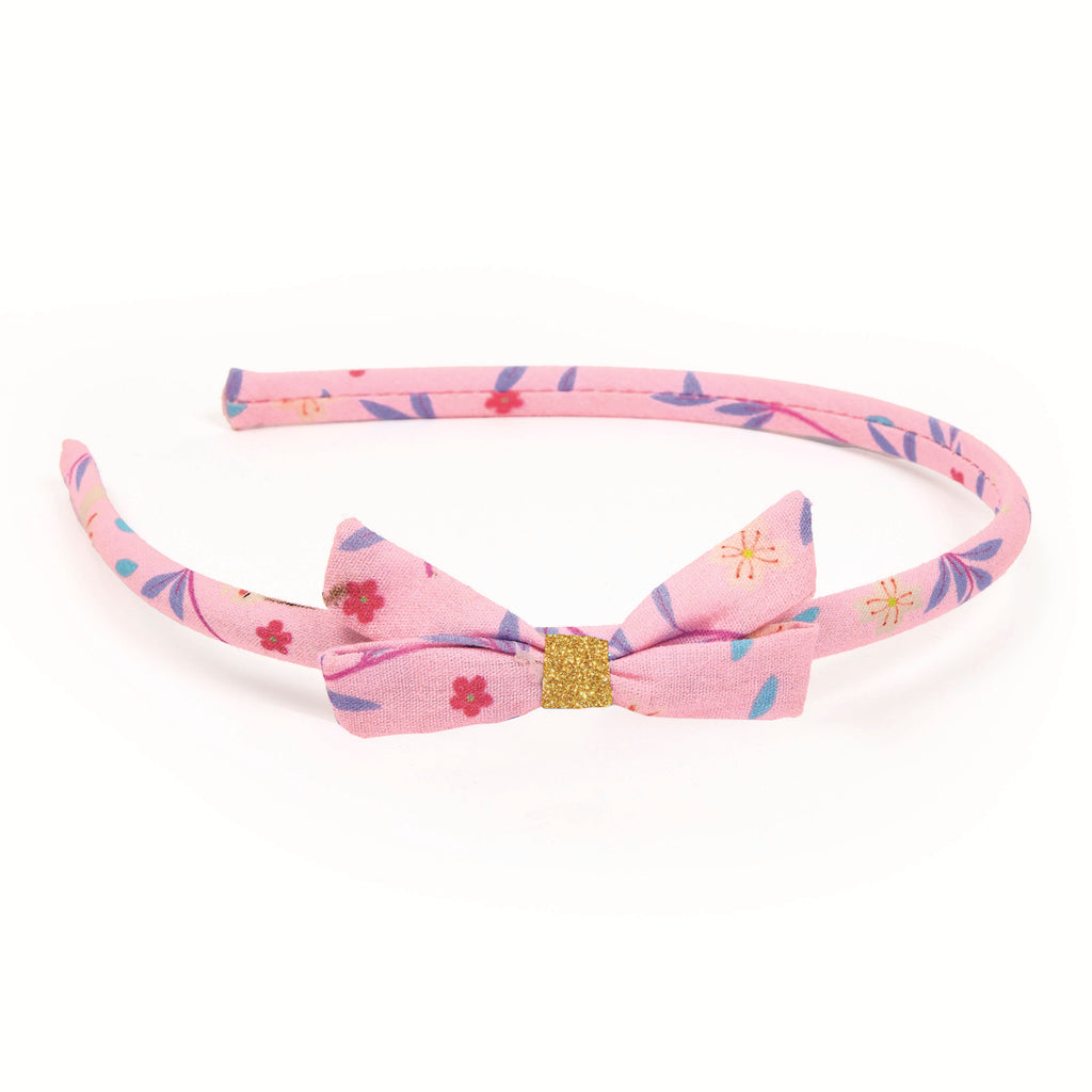 Pink floral headband with a matching bow featuring small flower designs in blue, red, and yellow. A gold glitter band accents the bow, conveying a playful and cheerful tone.