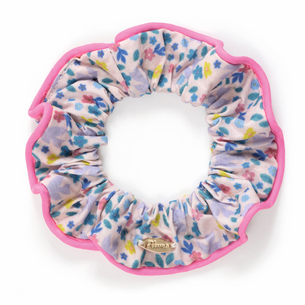 Floral scrunchie with bright pink edges, featuring blue and pink flowers on a light background. A small gold metal tag is attached.
