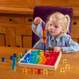 Young girl stacking colorful translucent discs in a wooden tray, sitting at a wooden table. She is focused and wears a light denim jacket.