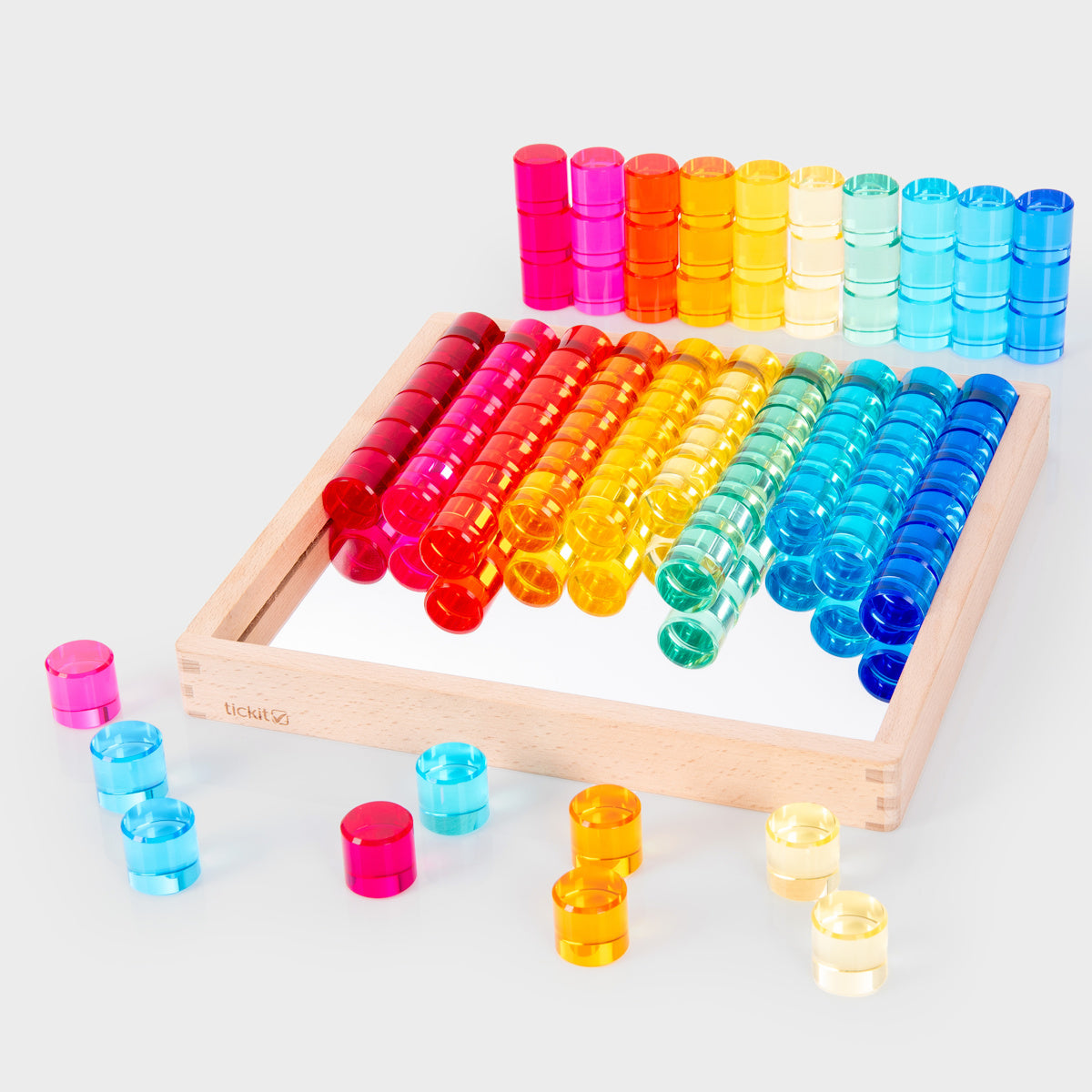 Colorful transparent counters in red, orange, yellow, green, and blue, arranged neatly on a mirrored wooden tray and scattered around it, creating a playful and vibrant tone.