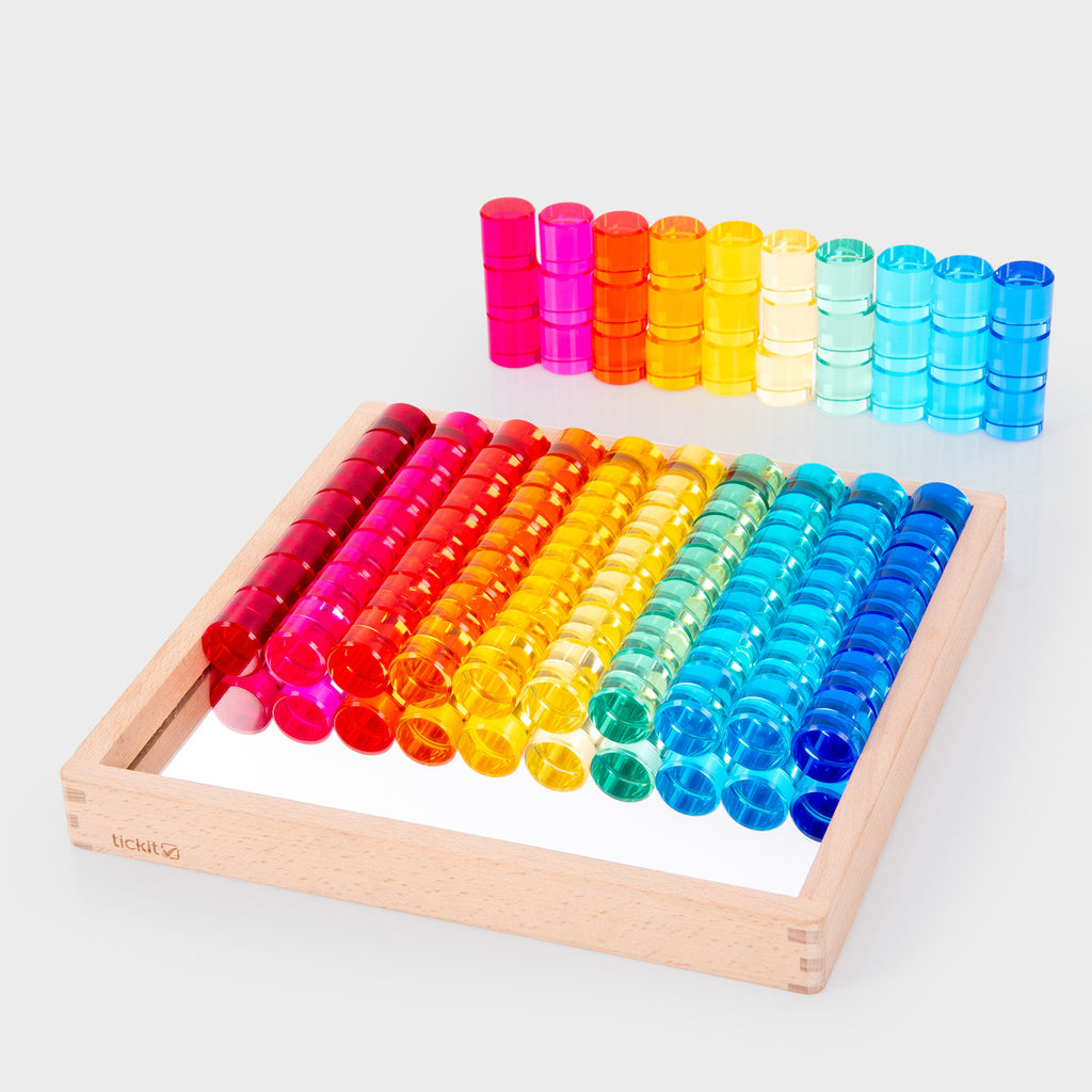 A wooden tray holds colorful transparent counters arranged in a vibrant rainbow pattern from red to blue, creating a bright and cheerful display.
