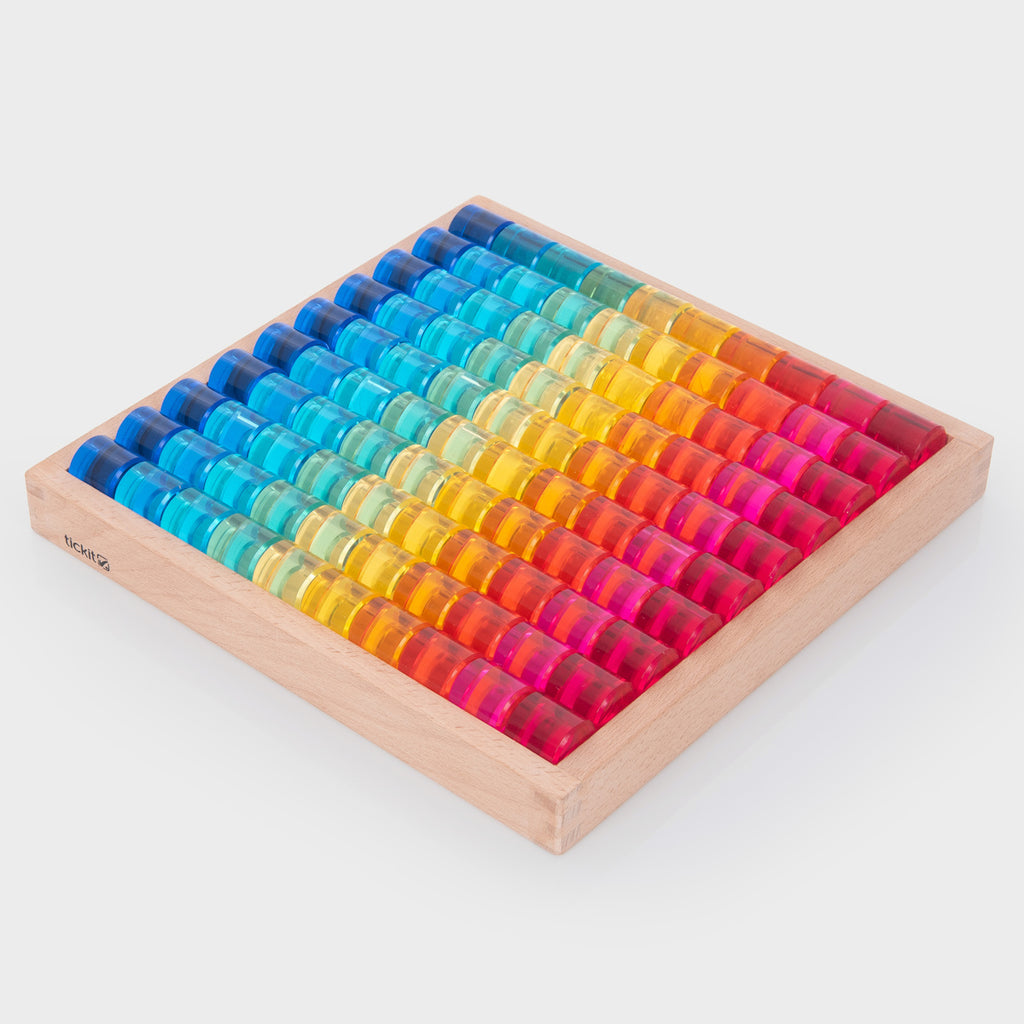 A wooden tray holds colorful transparent counters arranged in a vibrant rainbow pattern from red to blue, creating a bright and cheerful display.