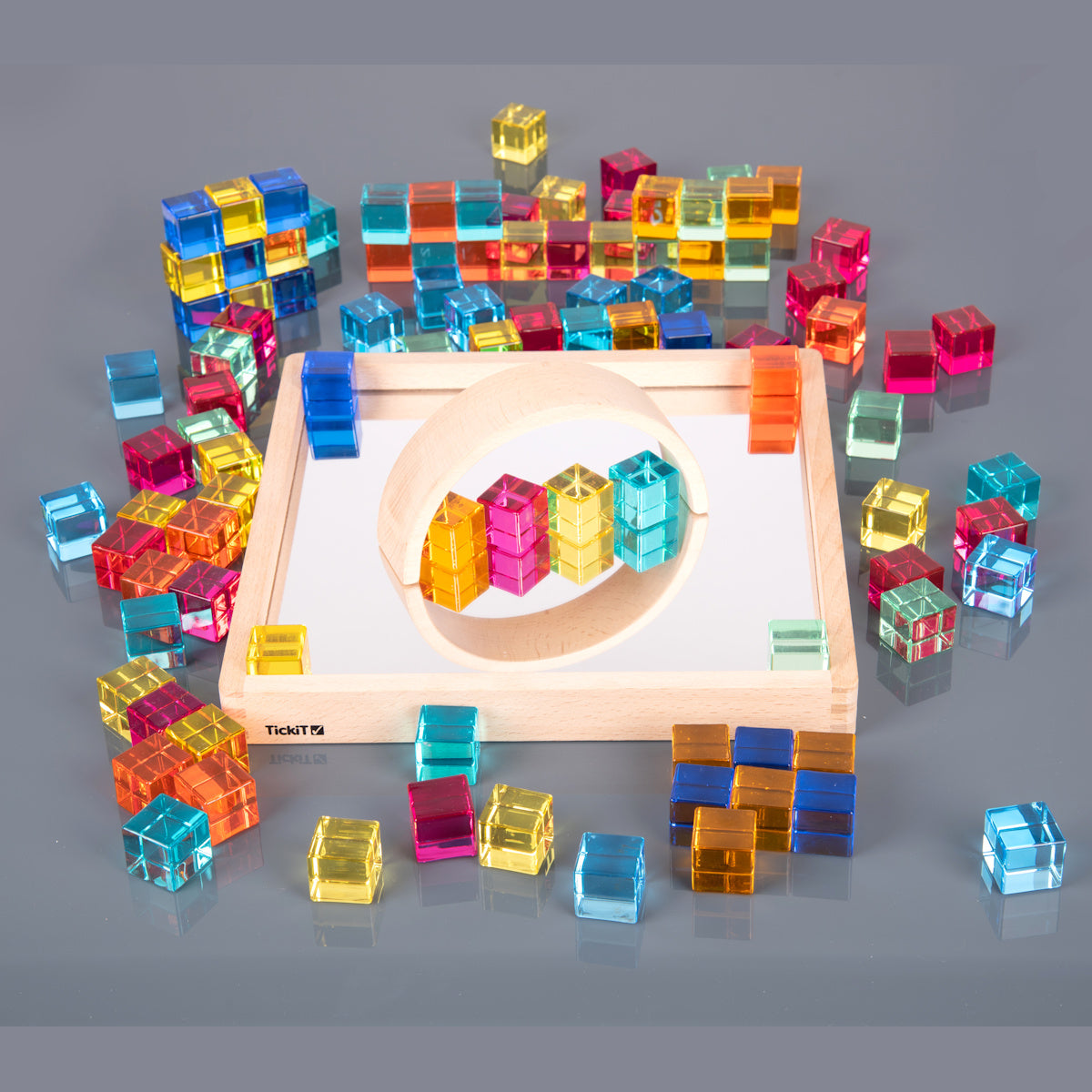 A square wooden tray with a mirrored base and colorful gem-like insets, designed to inspire sensory exploration, pattern making, and visual play.