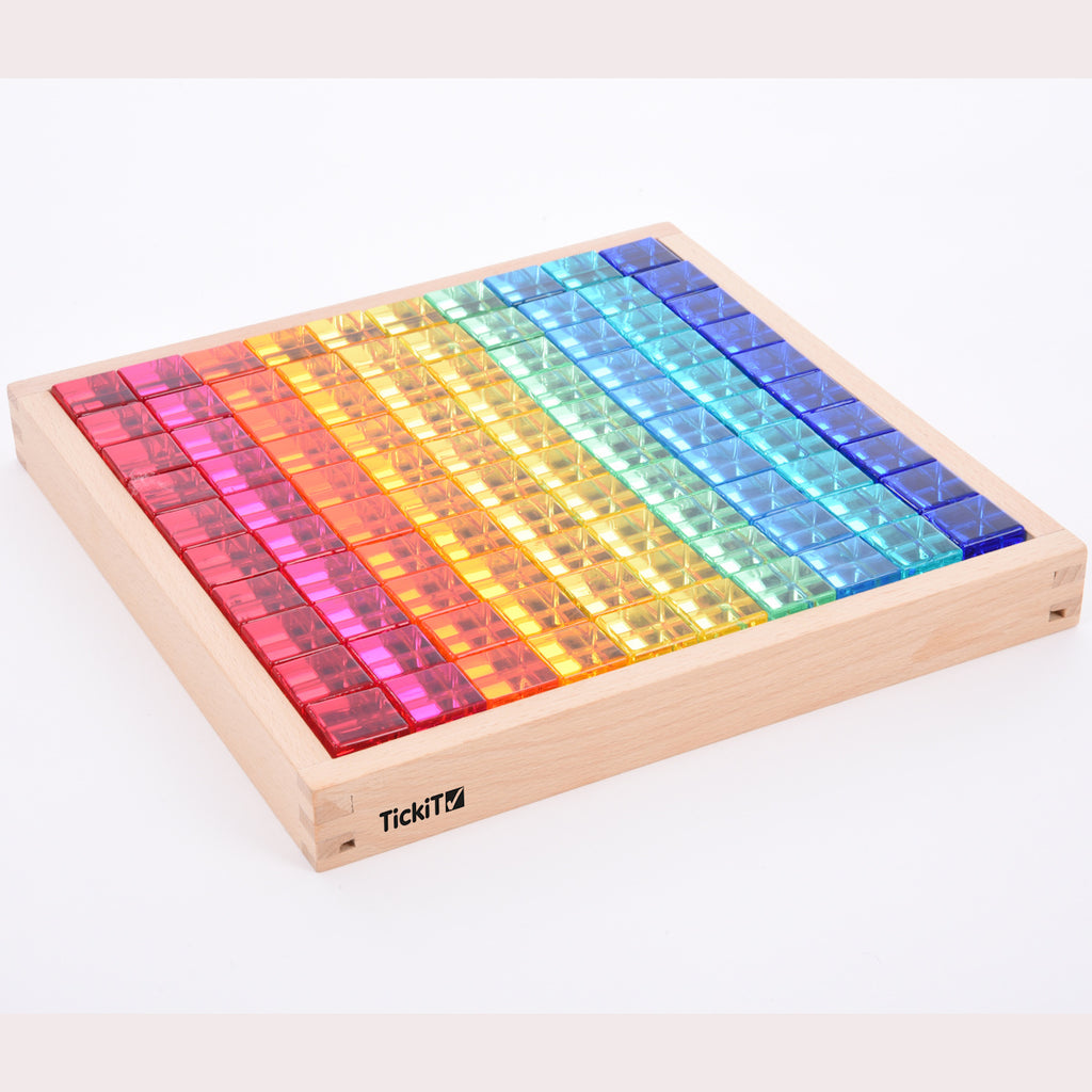 A square wooden tray with a mirrored base and colorful gem-like insets, designed to inspire sensory exploration, pattern making, and visual play.