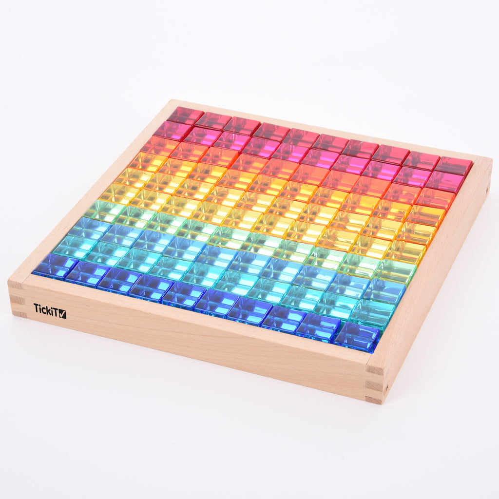 A square wooden tray with a mirrored base and colorful gem-like insets, designed to inspire sensory exploration, pattern making, and visual play.