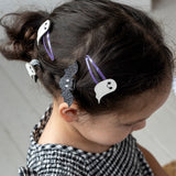 Young girl wearing glittery bat and ghost hair clips in her styled updo hair.