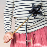 Child in striped shirt and pink skirt holding a black glittery star magic wand with ribbons.