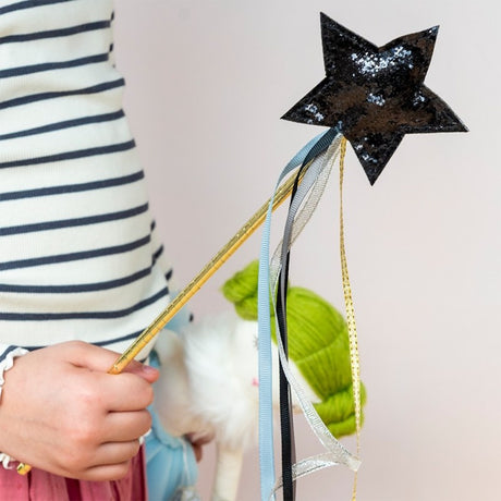 Child holding a black glittery star magic wand with colorful trailing ribbons.