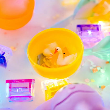 Miniature goose and farm figurines inside a yellow cup surrounded by colorful light-up sensory toys.