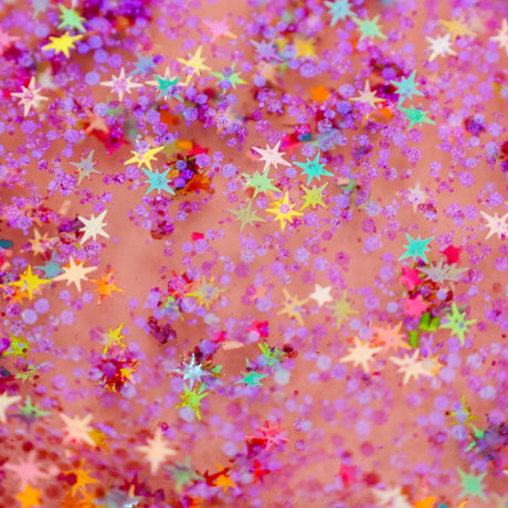 Close-up of colorful star-shaped confetti and purple glitter suspended in liquid.