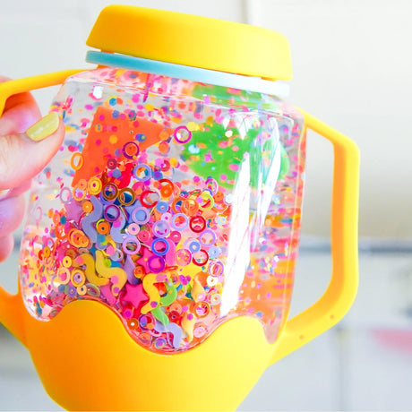 A yellow sensory jar filled with water, colorful sequins, confetti, and floating foam shapes.
