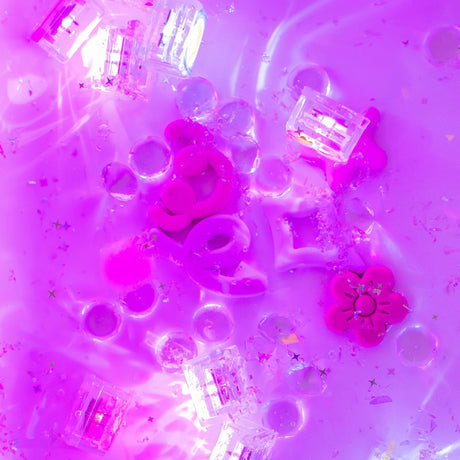 Light-up sensory cubes, pink shapes, and glitter submerged in glowing purple water.