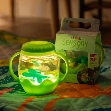 A glowing green mini sensory jar with handles filled with liquid, sitting next to its packaging box.