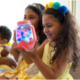 Young girl holding a glowing coral sensory jar filled with colorful liquid and shapes, smiling with delight.