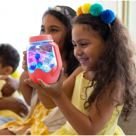 Young girl holding a glowing coral sensory jar filled with colorful liquid and shapes, smiling with delight.