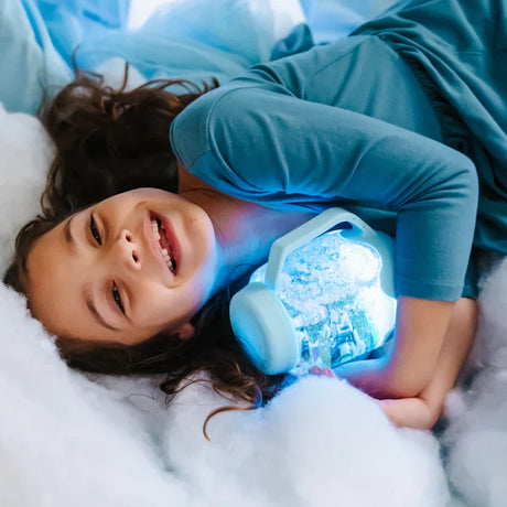 Smiling girl lying in soft white material, hugging a glowing light blue sensory jar.
