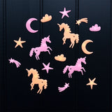 Pink and yellow glow-in-the-dark unicorn, star, and crescent moon shapes on a dark wall.