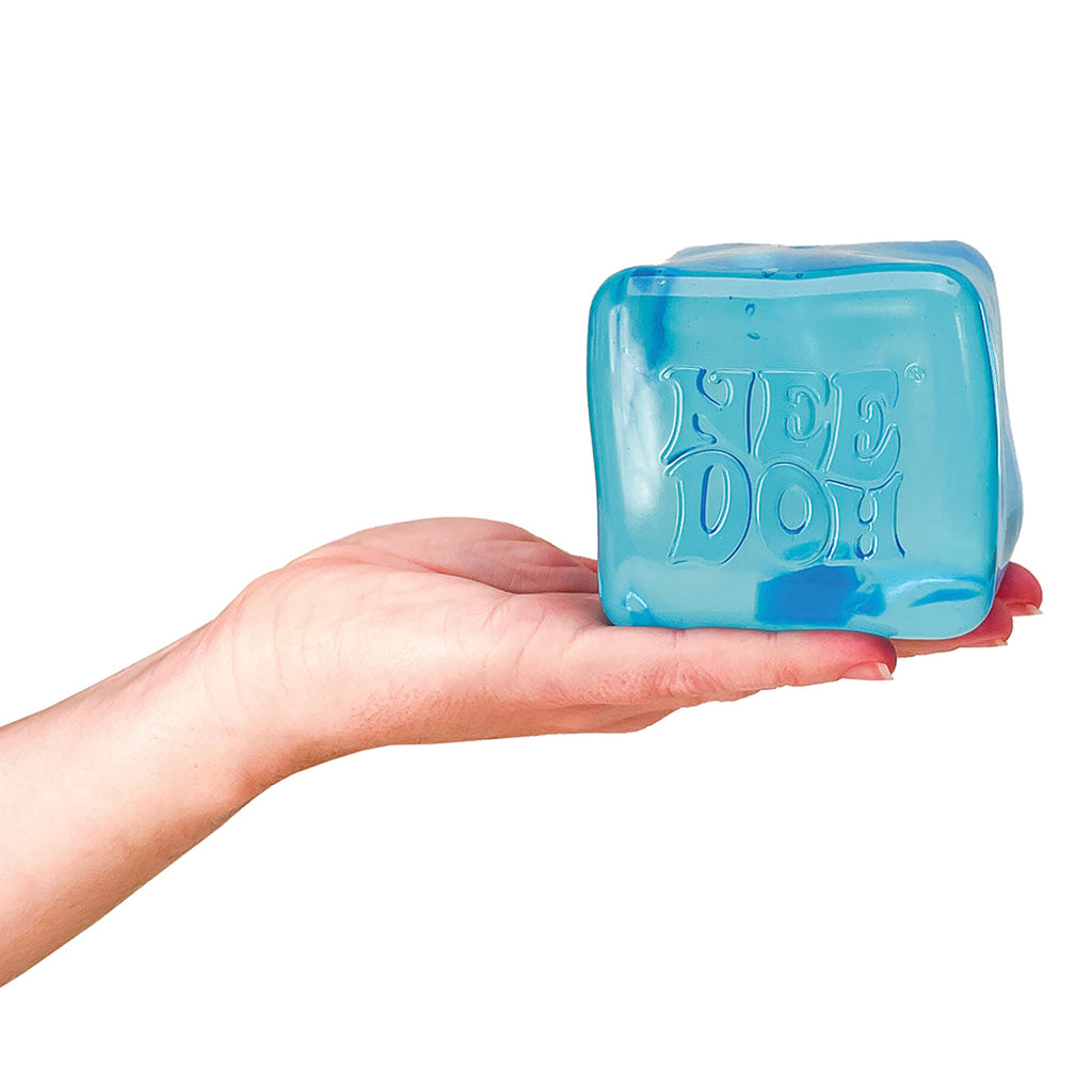 Hand holding a blue, cube-shaped stress ball with "NEE DOH" embossed on it. The image conveys a playful, calm, and tactile sensation.