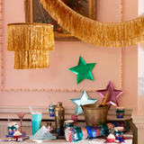 Gold tinsel chandelier hung above a festive party table set with metallic star plates and drinkware.