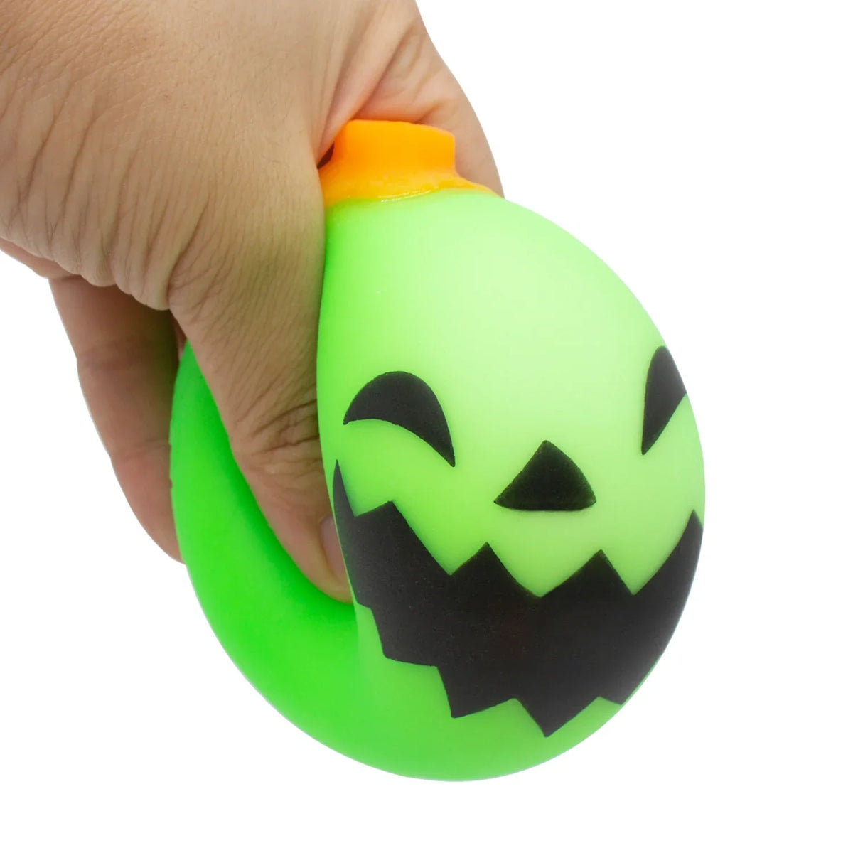 Hand squeezing a green Schylling NeeDoh Jack-Glow Lantern pumpkin squishy toy to show its stretchy, dough-like texture.