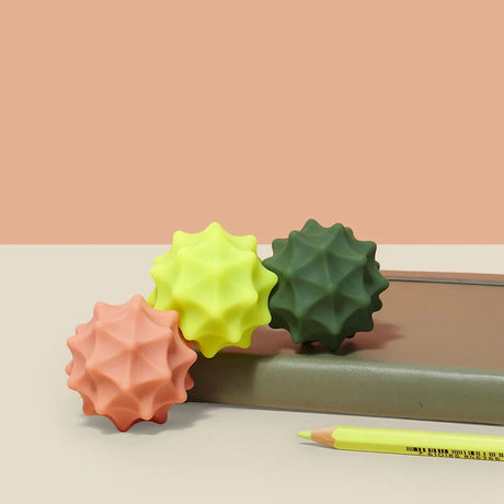 Three colorful spiky silicone magnetic fidget spheres resting near a notebook and pencil.
