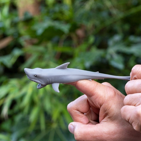 Grey stretchy rubber shark toy being pulled back on a finger like a catapult launcher.