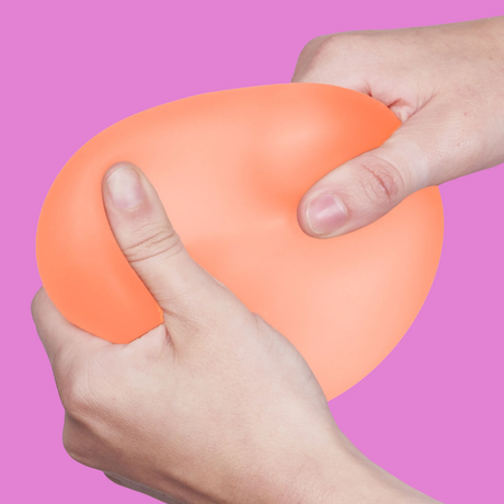 Two hands squeeze an orange stress ball against a vibrant pink background, conveying a sense of relief and tension release.