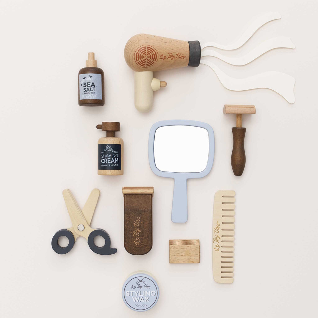 Toy barber set featuring wooden styling tools, a comb, mirror, and play hair products. The set conveys a playful, vintage barber theme.