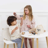 Two young children playing with a wooden hairdresser and barber kit set at a small table.