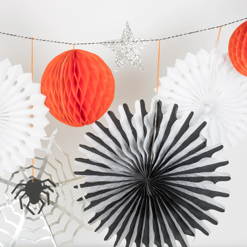 Colorful Halloween decorations on string, featuring orange honeycomb balls, a silver star, paper spider webs, and black and white fan shapes.