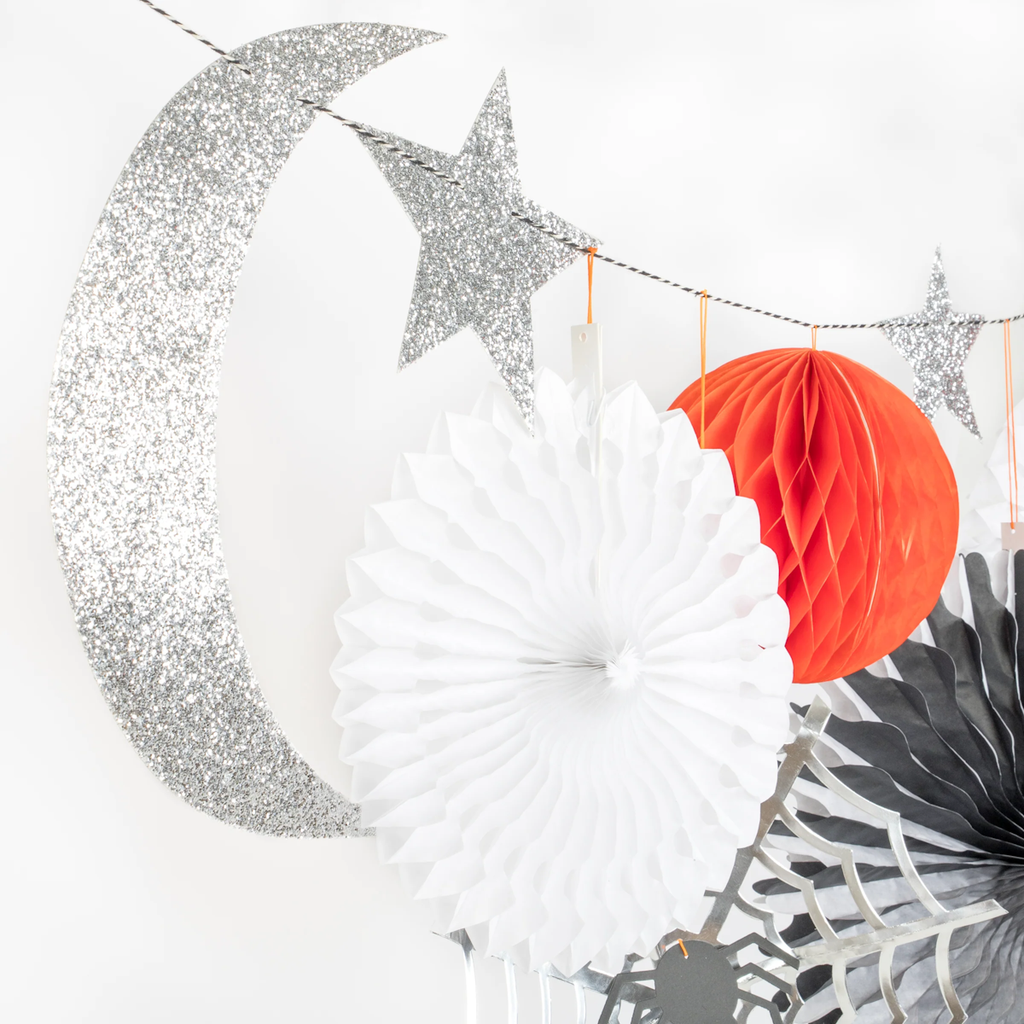 Glittery silver crescent moon and stars hang alongside white and red paper decorations on a string, creating a festive, cheerful ambiance.
