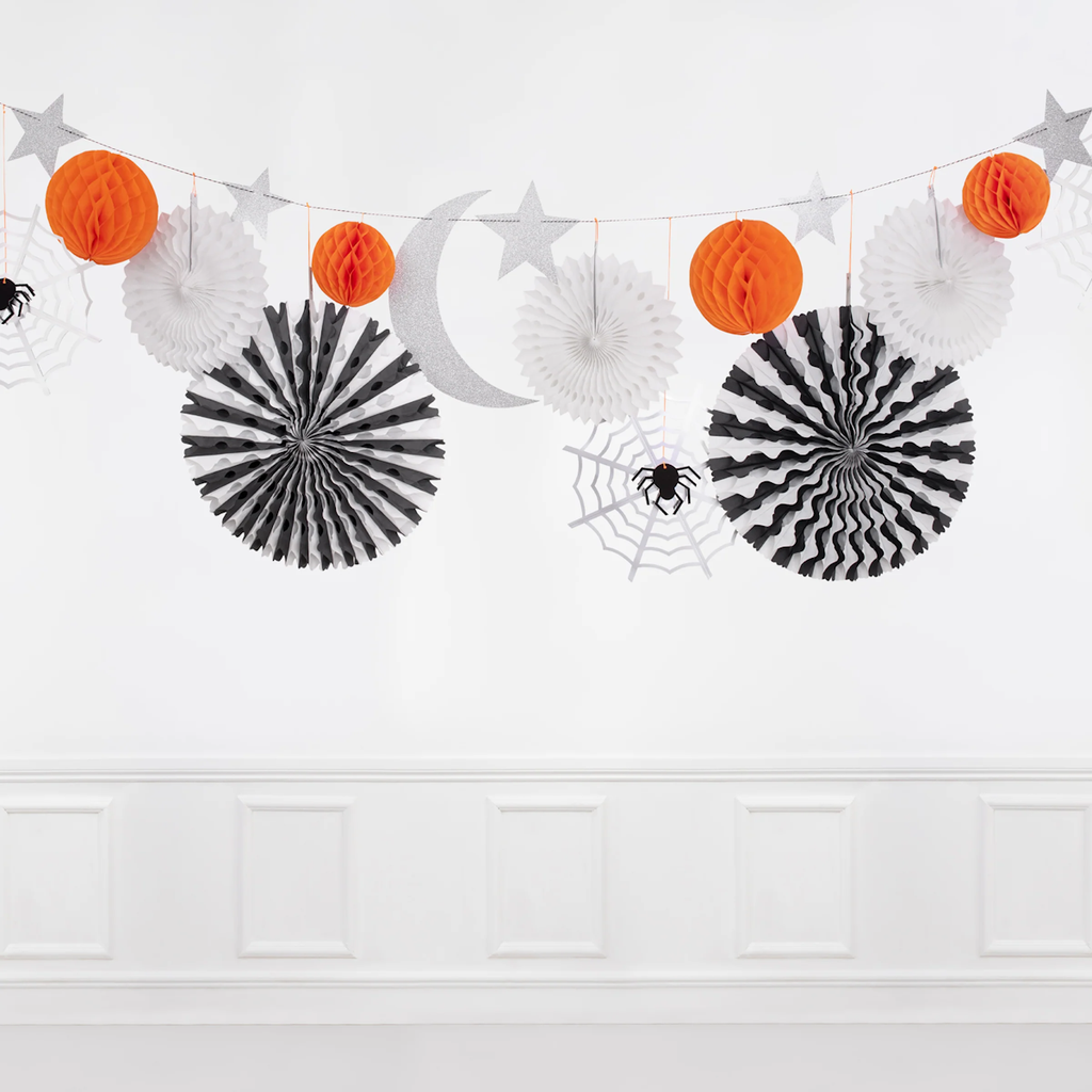 Halloween-themed decorations hang against a white wall, featuring orange and white paper fans, gray stars, a crescent moon, and spider webs.
